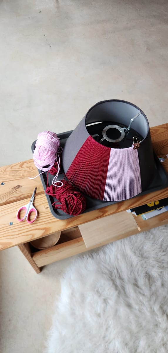 A black shade being wrapped in deep red and pink yarn