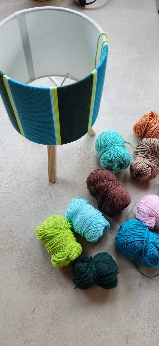 A finished teal and lime lamp beside leftover balls of yarn
