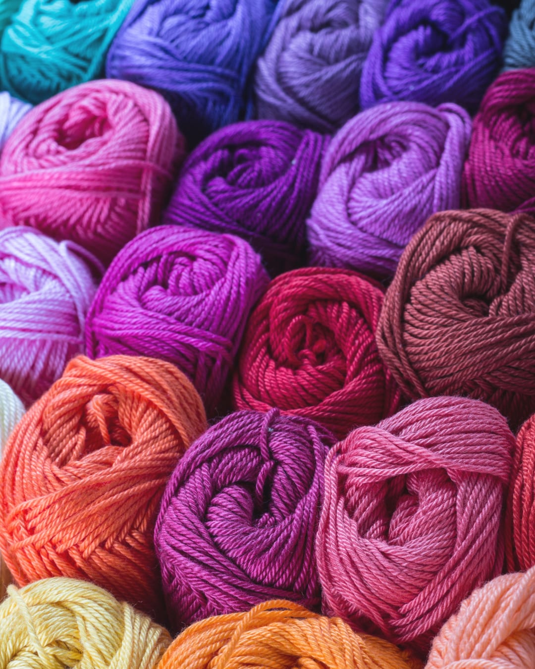 Dozens of balls of yarn in pinks, purples and oranges packed together