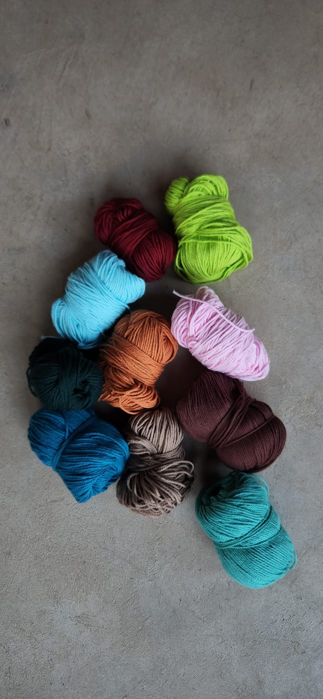 A dozen balls of yarn in bright colours on a concrete floor